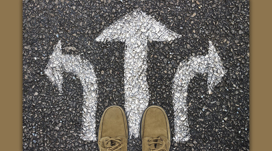 auf dem Boden sind drei weiße Kreide-Pfeile, die geradeaus, nach rechts und nach links zeigen. Die Schuhe, die zu sehen sind, suggerieren, dass es um eine Wahl geht.