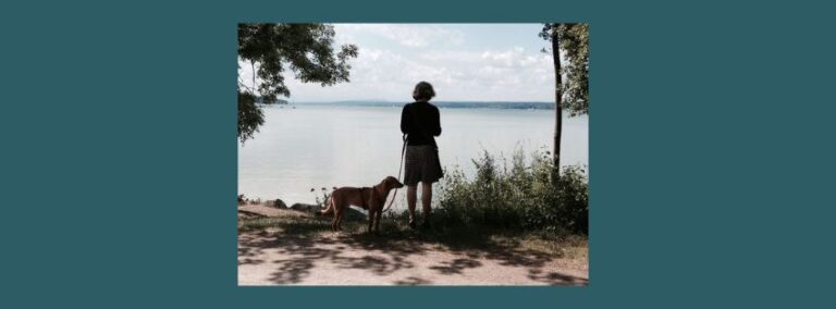 Frau steht am Ufer, hat einen Hund an der Leine – Leben halt