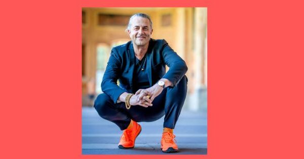 Veit Lindau, hockend mit orangefarbenden Sneakern und einem blauen Anzug