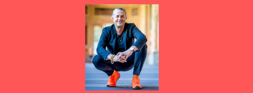 Veit Lindau, hockend mit orangefarbenden Sneakern und einem blauen Anzug