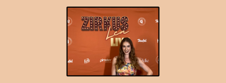 Die Artistin Lea Toran Jenner steht vor einer Wand, die ihre eigene Show Zirkus Lea Live promotet